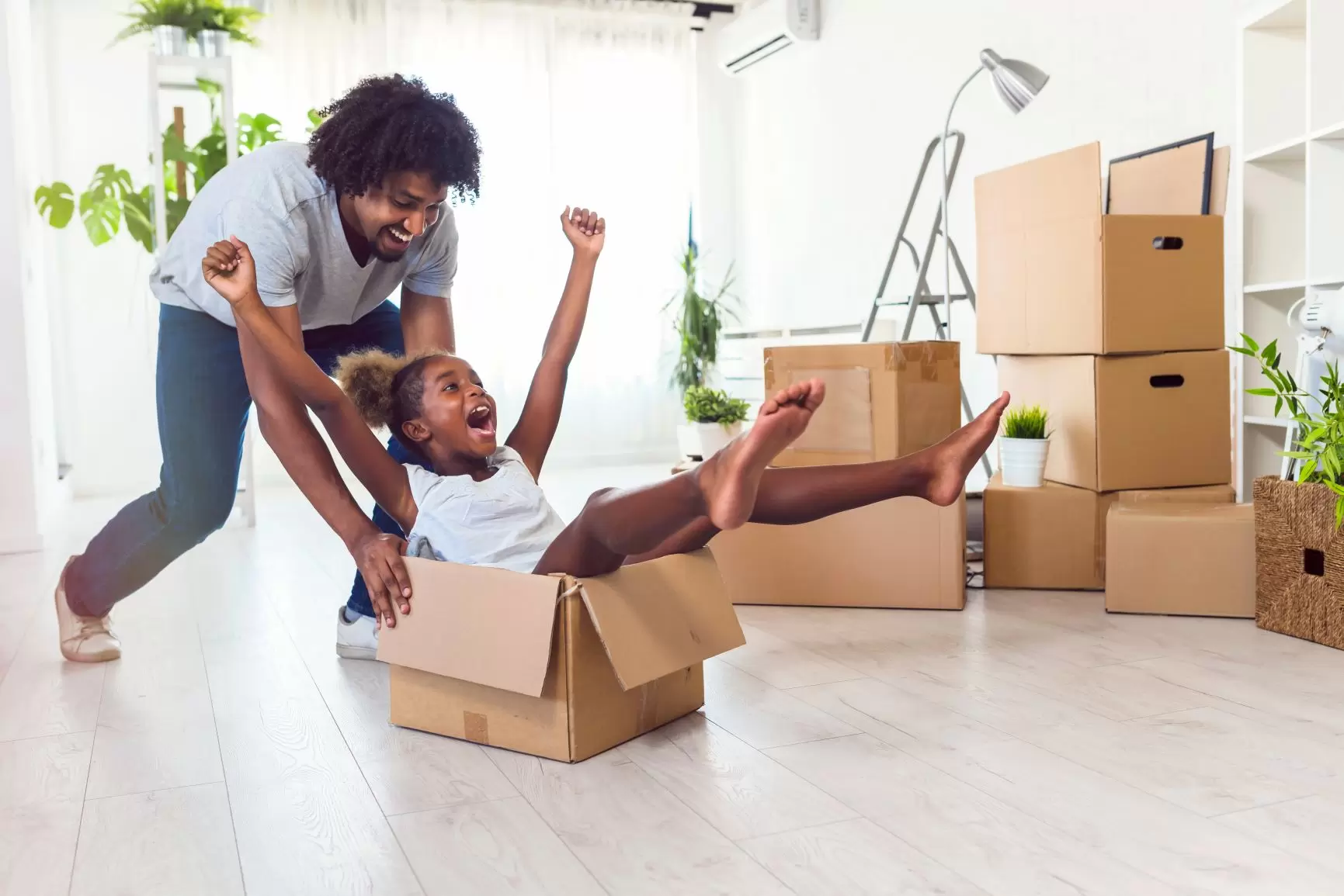 Father playing with daughter with moving boxes surrounding them.